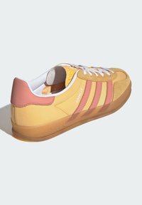 Zapatillas de ante y textil amarillas con acentos rosas, cordones blancos y suela de goma transparente, que cuentan con tres franjas diagonales y una marca en relieve.