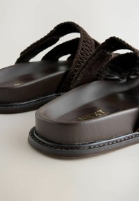 Zbliżenie na ciemnobrązowe klapki na grubych podeszwach z plecionymi paskami na jasnej powierzchni.