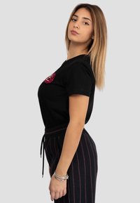 Maglietta nera in cotone a maniche corte, con una grafica testurizzata rosa sul petto. Abbinata a pantaloni da tuta neri a righe.
