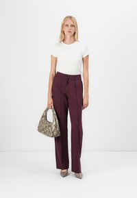 Chemise blanche à manches courtes, pantalon burgundy à jambe large avec cordon de serrage, portant un sac à main en imprimé serpentin et chaussée de chaussures à bout pointu beiges.