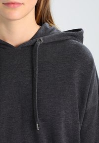 Felpa con cappuccio grigio carbone caratterizzata da un cappuccio con coulisse, una consistenza morbida e una vestibilità rilassata. Include dettagli in metallo silver per gli accenti della coulisse.