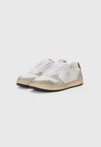 Hvite sneakers med grå semsket skinn og lærdetaljer. Har perforert tå, hvite snøringer og gulllogo på siden. Svart gummisåle.