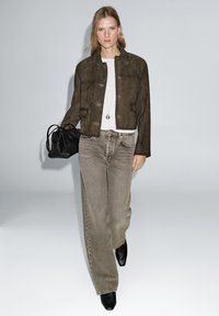 Cropped brown suede jacket, beige top, faded gray wide-leg jeans, and black ankle boots; holding a small black handbag.