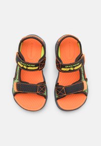 Svarte og oransje sandaler med justerbare velcro-remmer, teksturerte såler og grønne detaljer. Lettvektsdesign for komfort og støtte.