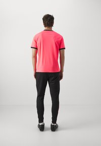 Kortvingerige, felroze T-shirt met zwarte afwerking, gecombineerd met zwarte sportbroek met rode accenten en een slim fit ontwerp.