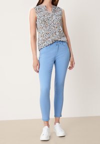 Top sin mangas con estampado floral en azul claro; combinado con vaqueros ajustados azul claro; completo con zapatillas blancas.