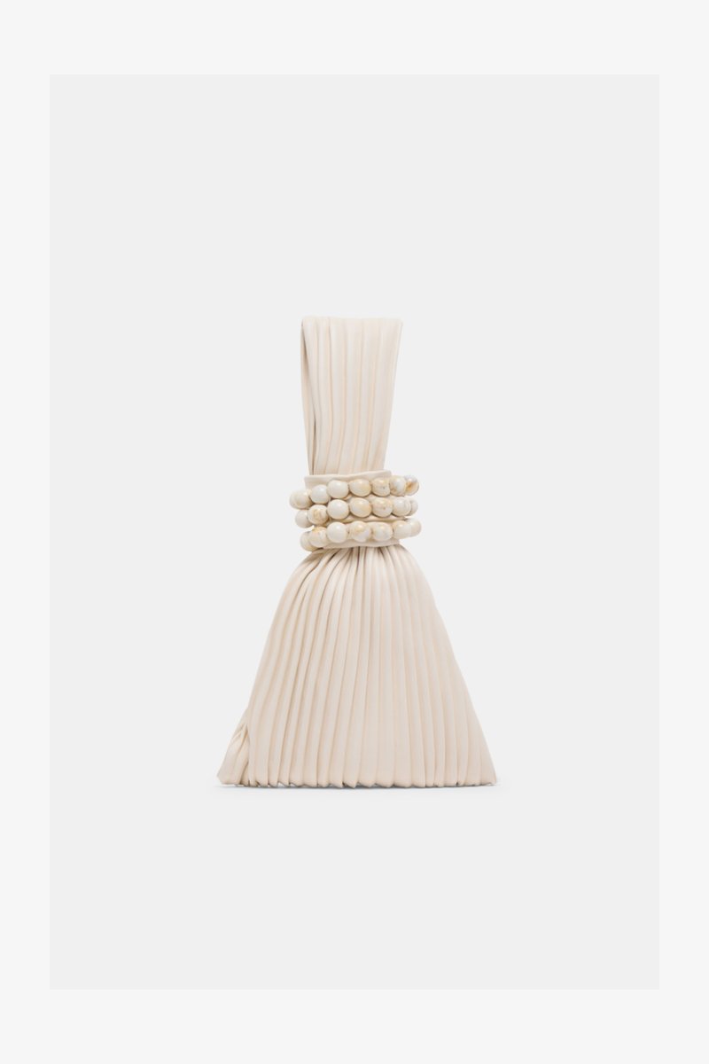 Μικρό μπεζ τσάντα με πιέτες, χειρολαβή με κόμπο και τρία στρογγυλά βραχιόλια από χάντρες τυλιγμένα στη μέση.