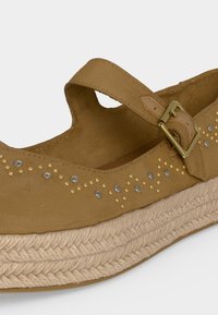 Chaussure Mary Jane marron avec détails cloutés, bride à boucle et semelle tressée style espadrille.