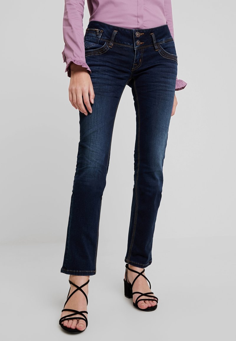 Mörkblå denimjeans med kontrasterande sömmar, midjehöjd och slim fit-design. Kombineras med svarta remsandaler.