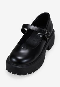 Zapato Mary Jane de charol negro con punta redonda, correa ajustable y suela de plataforma negra gruesa y texturizada.