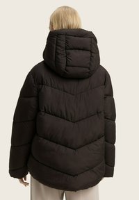 Zwarte pufferjack met een capuchon, voorzien van een chevron-quiltpatroon, dikke vulling en elastische manchetten voor warmte en comfort.