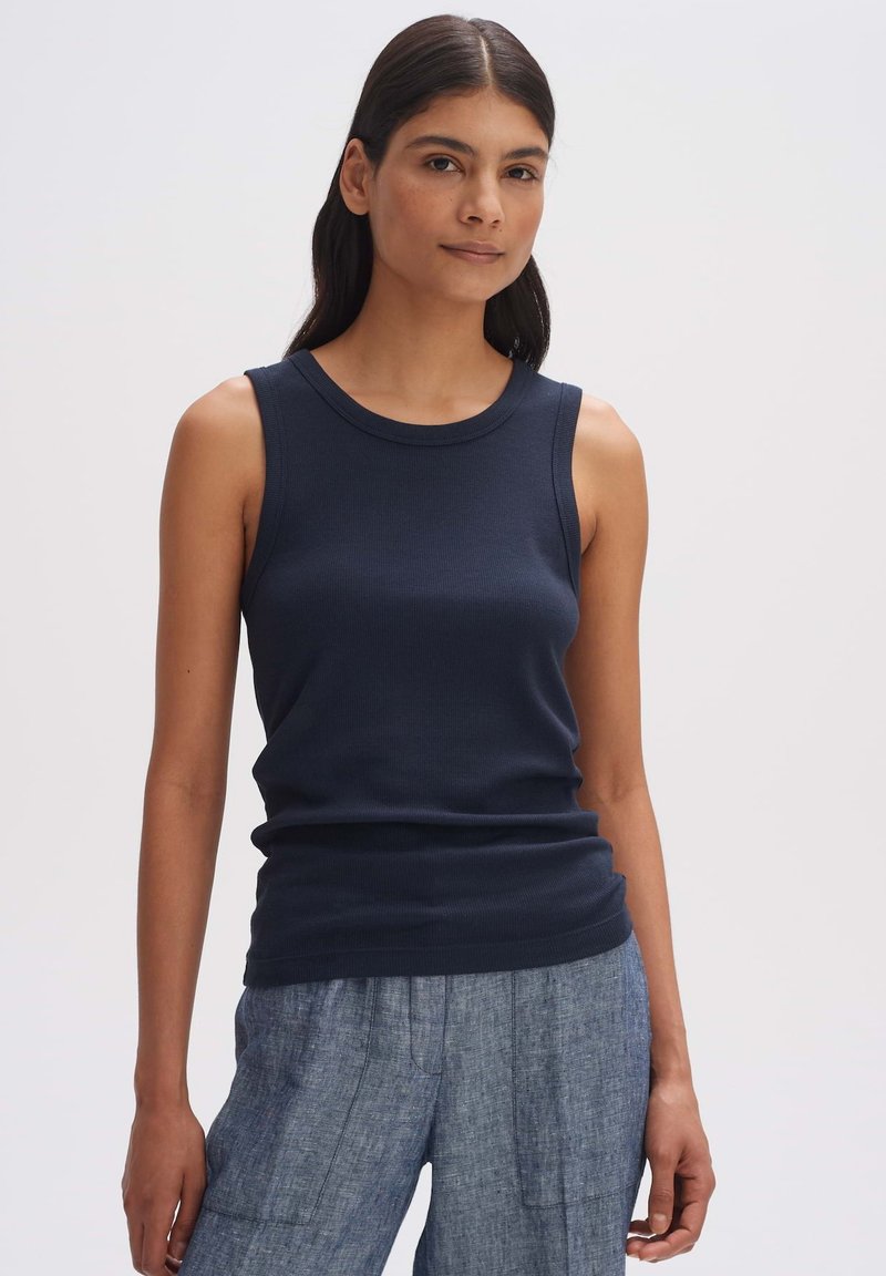 Top a canotta a coste blu navy con scollo rotondo e spalline larghe, abbinato a pantaloni grigi chiari texturizzati.