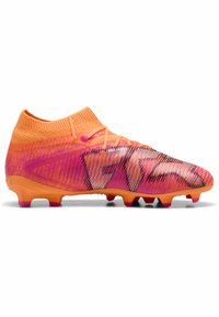 Scarpini da calcio arancioni e rosa con una tomaia texturizzata, colletto in tessuto a maglia e strisce nere in contrasto. Presentano una suola in gomma chiodata.