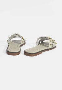 Witte platte sandalen met gouden studs; open teen ontwerp, verstelbare bandjes, gevoerde inlegzool en een bruine rubberen zool.