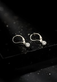 Orecchini a cerchio in argento con pietre circolari trasparenti, che mostrano una finitura lucida e un design elegante su uno sfondo scuro.
