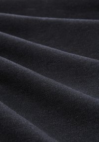 Schwarzer Stoff mit einer weichen Textur, der sichtbare diagonale Webmuster aufweist, die in wellenförmigen Falten angeordnet sind.