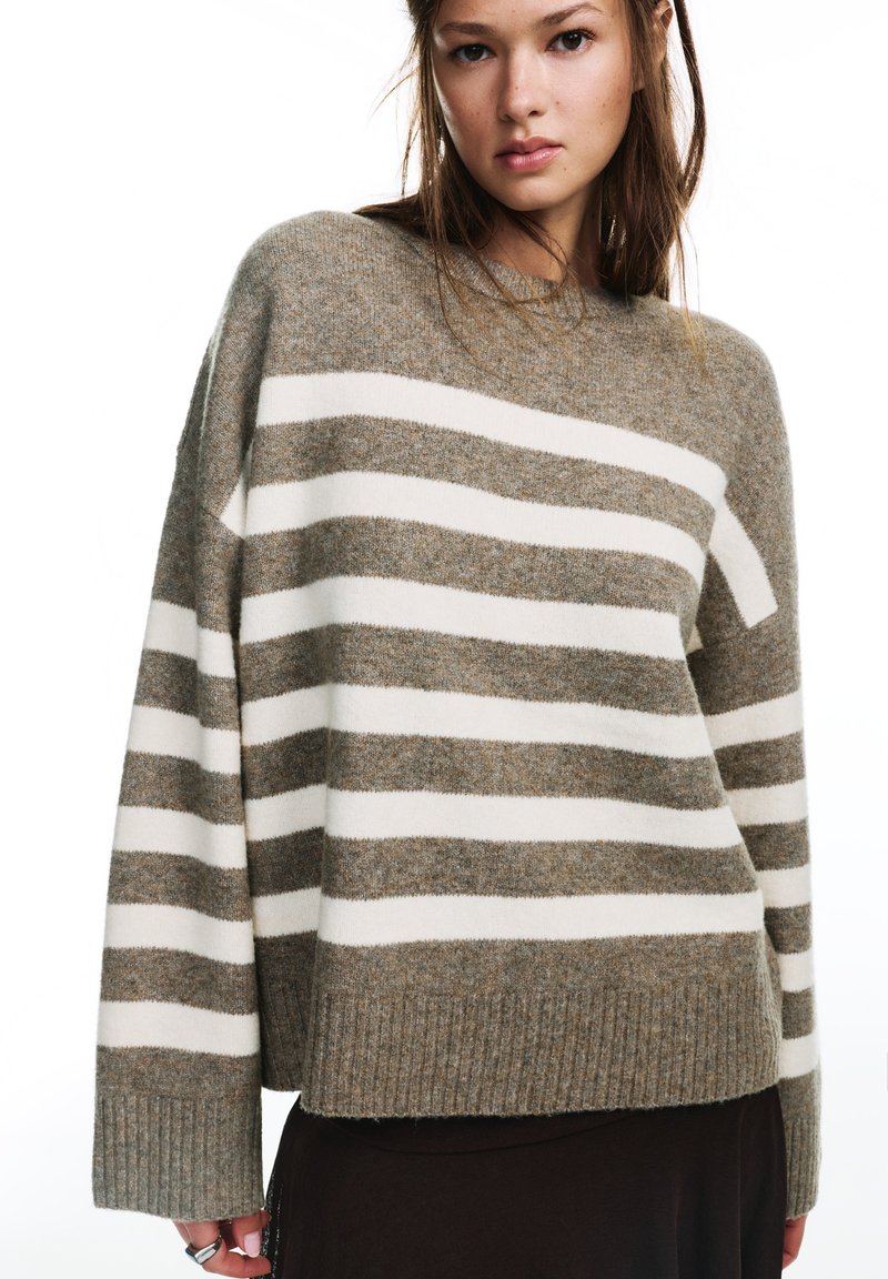 Pull rayé beige et crème, en matière douce. Il présente un col rond, des poignets et un ourlet côtelés, avec une coupe décontractée.
