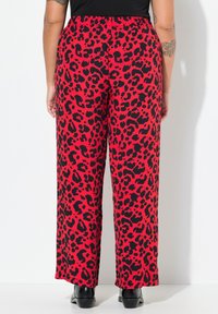 Rode broek met een zwart luipaardprintpatroon, wijde pijpen, elastische tailleband en omgezoomde randen. Gedragen met zwarte schoenen.