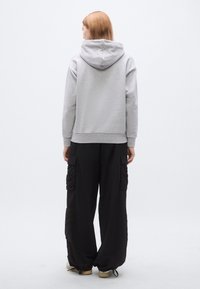 Halli dressipluus kapuutsiga, millel on nööriga kapuuts, soonikkoes varrukad ja alläär, kombineeritud lahtiste mustade taskutega pükstega, millel on küljetaskud ja matt tekstuur.