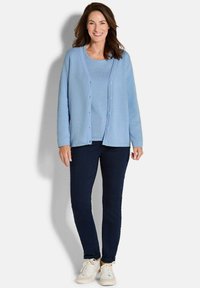 Hellblauer strukturierter Cardigan mit Knöpfen, kombiniert mit einem passenden Pullover, dunklen Hosen und weißen Sneakern. Minimalistisches Design, lässige Passform.