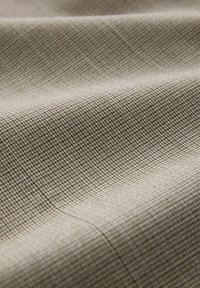 Tela textil con un patrón de cuadrícula en beige y marrón, con una textura suave y un ligero brillo, dispuesta en pliegues suaves.