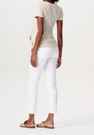 Beige top met korte mouwen en een afgeronde zoom, gecombineerd met witte slim-fit broek en bruine sandalen. Gladde stof met subtiele textuur.