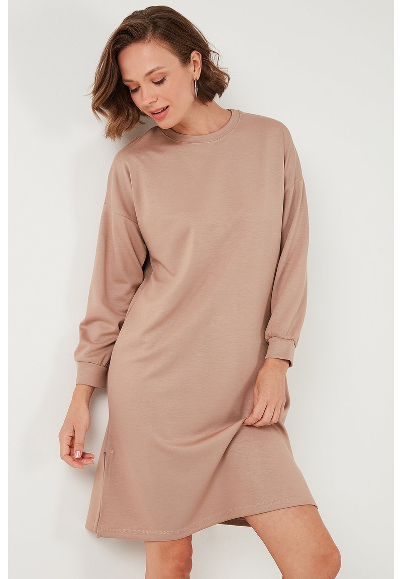 Long-sleeve beige dress made from soft fabric, featuring a round neckline, loose fit, and side slits at the hem for ease of movement.