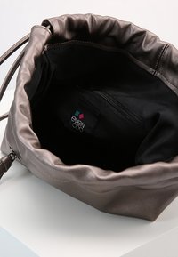 Hnědá umělá kožená kbelíková taška se staženým vrškem, černým interiérem, zipovou kapsou a s visačkou loga uvnitř. Hladký povrch a kulatý tvar.