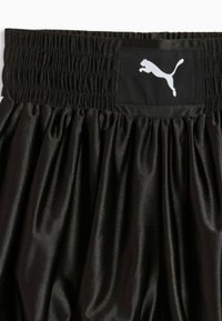 Ceinture élastique noire avec détail smocké et un patch rectangulaire noir présentant un logo Puma blanc sur un tissu noir froncé en dessous.