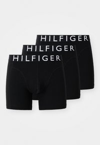 Tre svarte boksertruser for menn med hvite midjebånd merket "HILFIGER", lagt overlappende på en hvit bakgrunn.