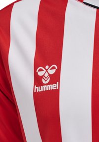 Rød og hvid stribet sportsjersey med en glat tekstur, der har et centralt logo af en stiliseret bi og mærkenavnet "hummel."