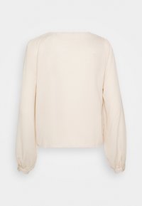 Hellbeige Bluse mit langen Ärmeln, runder Halslinie, leicht verkürztem Design und gerafften Bündchen mit Knöpfen an den Handgelenken. Glatte Textur.
