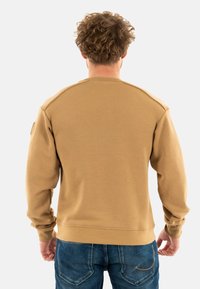 Felpa in cotone marrone con scollatura rotonda, polsini e orlo a costine. Presenta una texture liscia e una vestibilità comoda, indossata con jeans blu.