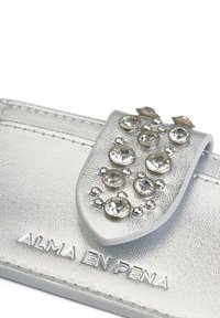 Portafoglio in pelle argentata con finitura testurizzata, caratterizzato da strass trasparenti decorativi e dettagli metallici sulla patta. Nome del marchio inciso alla base.