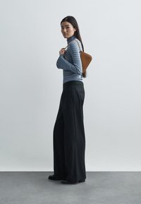 Csíkos kék garbó, széles fekete csíkos nadrág és egy barna bőr válltáska láncos pánttal, egy egyszínű háttér előtt.