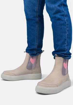 Beige ankelstøvler med tykke hvide såler og lyserøde hjerter på grå sidepaneler, båret med blå jeans.