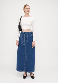 Lang denimskjørt med knyttet livbelte, blå farge, og frontknapplukking. Kombinert med et tettsittende hvitt langermet topp.