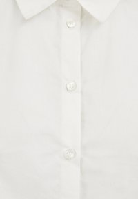 Valkoinen kauluspaita, jossa on sileä kangas, napit edessä, näkyvissä neljä nappia ja siististi taitettu kaulus. Yksinkertainen muotoilu, ilman kuvioita.