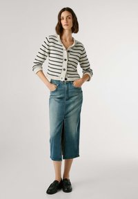 Gestreepte, roomkleurige en marineblauwe gebreide cardigan met knopen, gecombineerd met een lichtblauwe denimrok tot de knie met een split aan de voorkant en zakken.