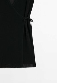 Zwarte gebreide omslag met een zijriemsluiting en een textuurpatroon tegen een effen witte achtergrond.