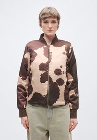 Καφέ και μπεζ bomber μπουφάν με μοτίβο από καφέ αγελάδας, με φερμουάρ μπροστά και ριμπ μανσέτες, κατασκευασμένο από γυαλιστερό σατέν ύφασμα.