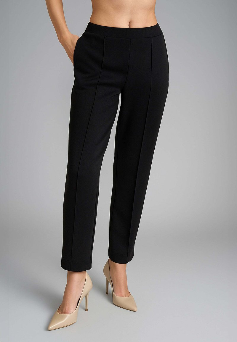 Pantaloni neri sartoriali con una superficie liscia, dotati di una vita aderente e tasche laterali, abbinati a décolleté beige a punta.