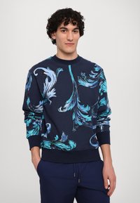 Granatowy sweatshirt z niebieskim wzorem kwiatowym, okrągły dekolt, ściągacze przy rękawach i u dołu, wykonany z miękkiej, bawełnianej tkaniny. Luźny krój.