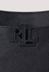 Melnā teksturētā ādas soma ar reljefā „RL” logotipa izspiedumu kontrastējošā apdarē augšpusē. Vienkāršs, elegants dizains bez rotājumiem.