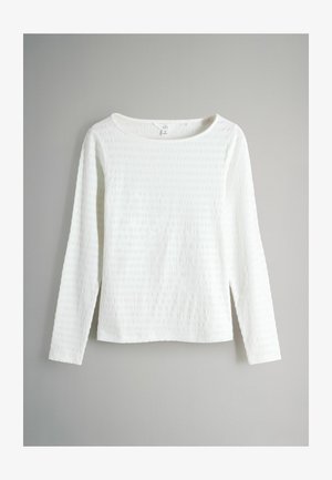 Fehér hosszú ujjú felső texturált anyagból, széles nyakkivágással és egyenesen szabott fazonnal. Az anyag finom mintázott dizájnt mutat.