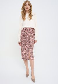 Bloemige midi rok met een split, met een kleurrijk bloemenpatroon op een zachte stof. In combinatie met een crèmekleurige gebreide trui en nude hakken.