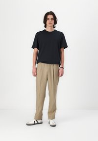 Camiseta de algodón negra con cuello redondo, combinada con pantalones de traje claros y con pinzas en color marrón claro y deportivas blancas con detalles en negro.