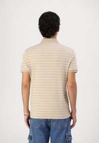 Beige gestreepte polo met korte mouwen, een kraag en een zachte textuur. De strepen zijn wit, wat een subtiel contrast creëert.