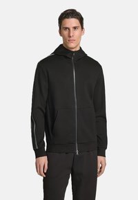 Felpa nera con zip realizzata in tessuto liscio, dotata di tasca a marsupio, polsini aderenti e strisce a contrasto lungo le maniche.