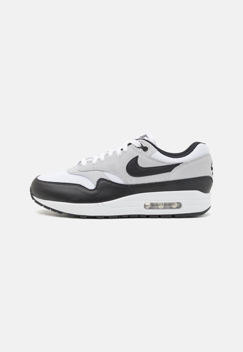 Nike Air Max 1 sneaker featuring a white and grey upper with black leather accents, rounded shape, and visible air cushioning in the sole.